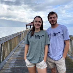 A male and female are smiling at the camera. The female is wearing a green "Got Litter?" t-shirt and the male is wearing a grey "Got Litter" t-shirt. They are standing on a wooden pier.