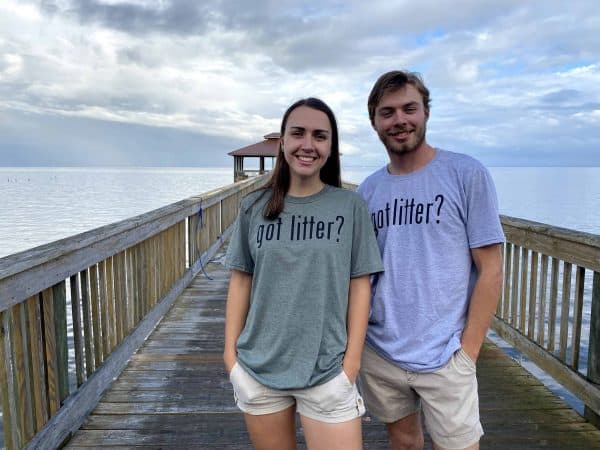 A male and female are smiling at the camera. The female is wearing a green "Got Litter?" t-shirt and the male is wearing a grey "Got Litter" t-shirt. They are standing on a wooden pier.