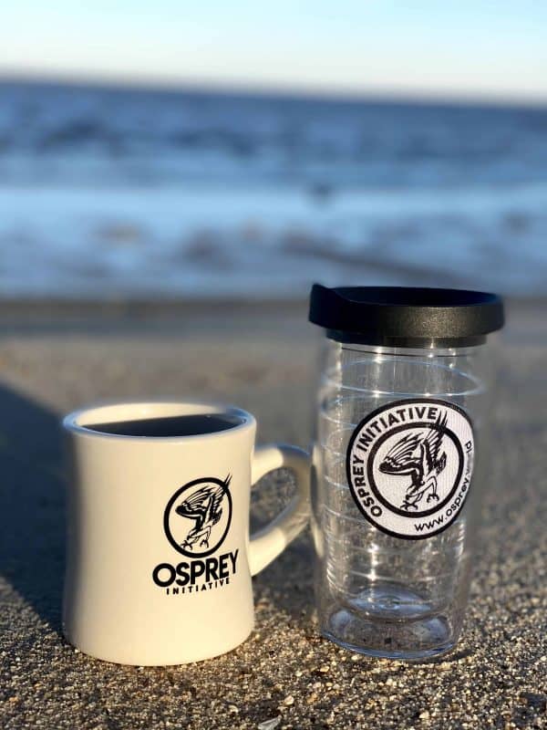 The Osprey tumbler and diner mug are positioned beside each other on the beach, with water in the background.